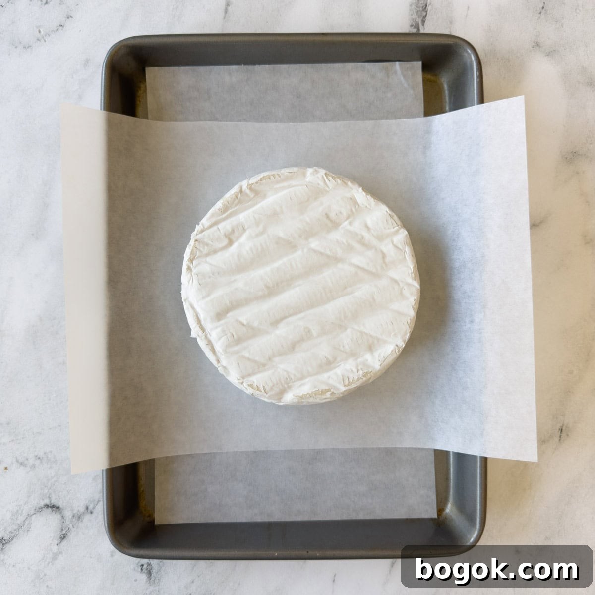 A round wheel of brie cheese on parchment paper on a baking sheet.