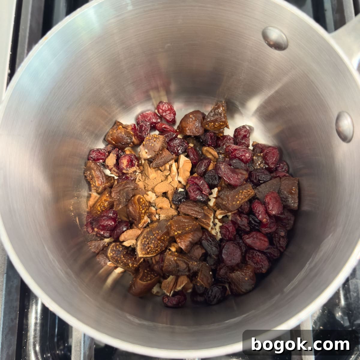 Dried cranberries, dried figs, nuts, and spices in a silver pot.