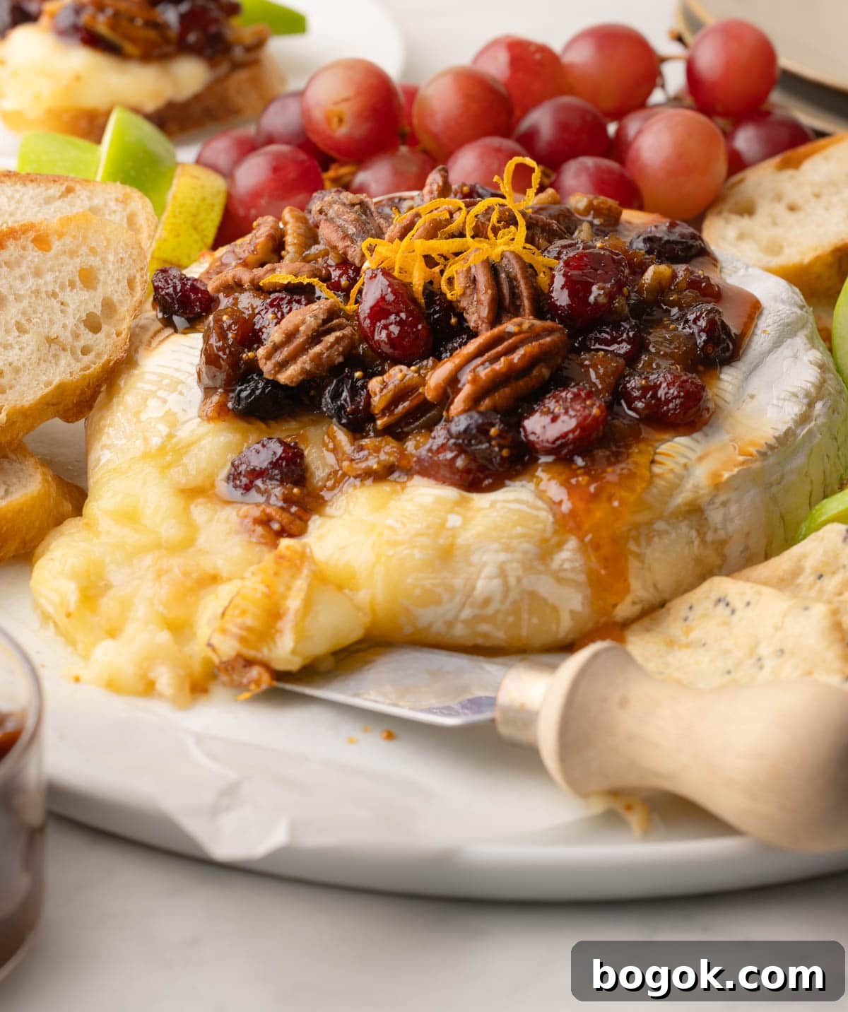 Warm brie cheese oozing out of the wheel on a platter topped with fruit and nut sauce.