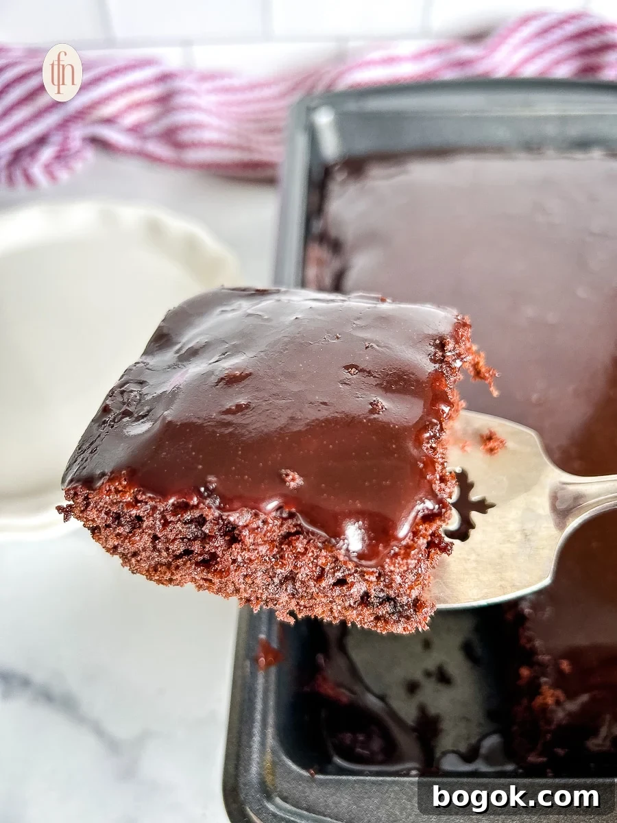 Dr Pepper Chocolate Sheet Cake Recipe - Moist Soda Cake Tutorial 8 Silver serving spoon holding slice of cake over the pan of chocolate Dr Pepper cake.