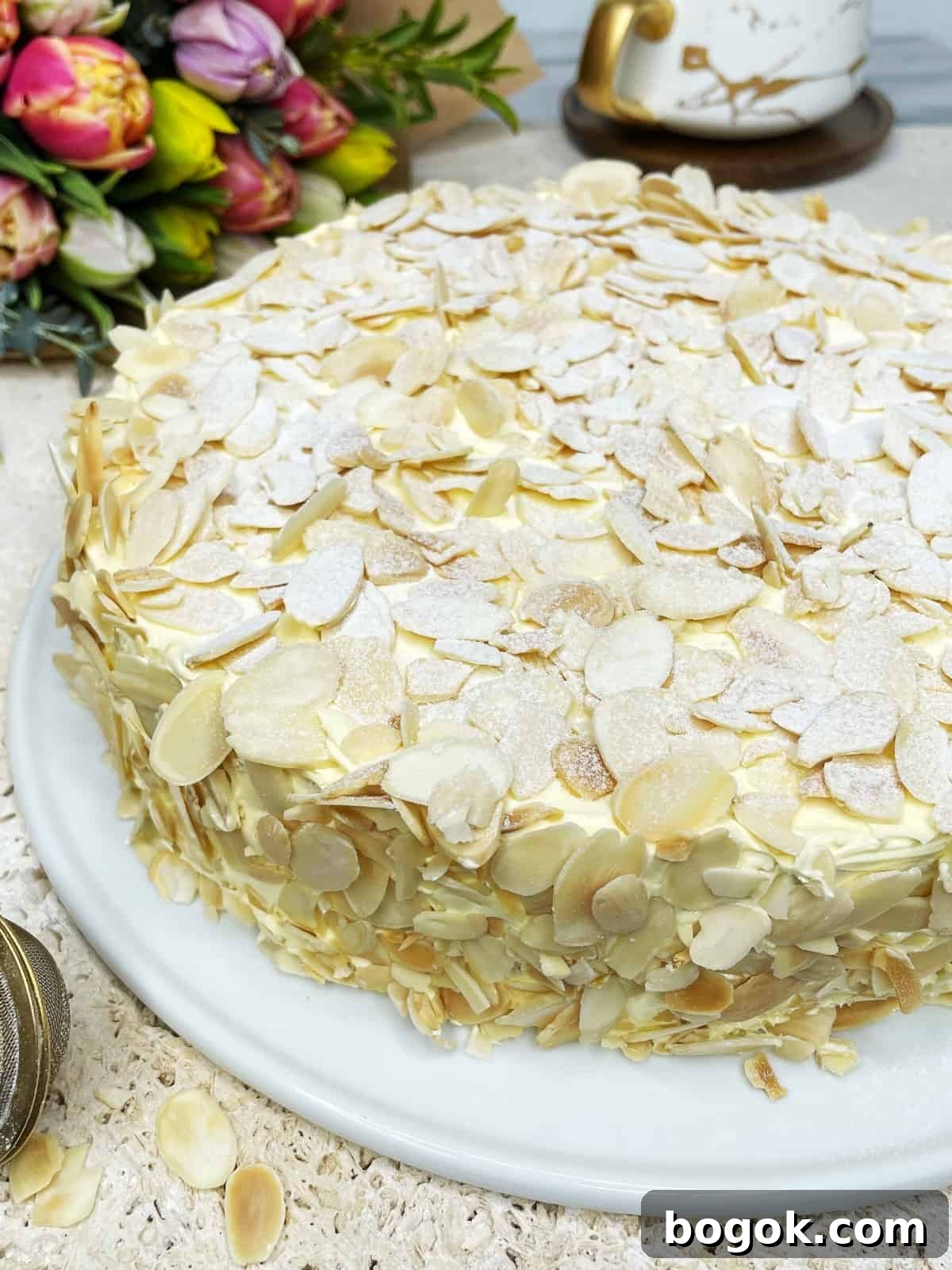 Authentic Gluten-Free Italian Almond Cake Recipe 3 Almond dacquoise cake topped with sliced almonds with a cup in the background