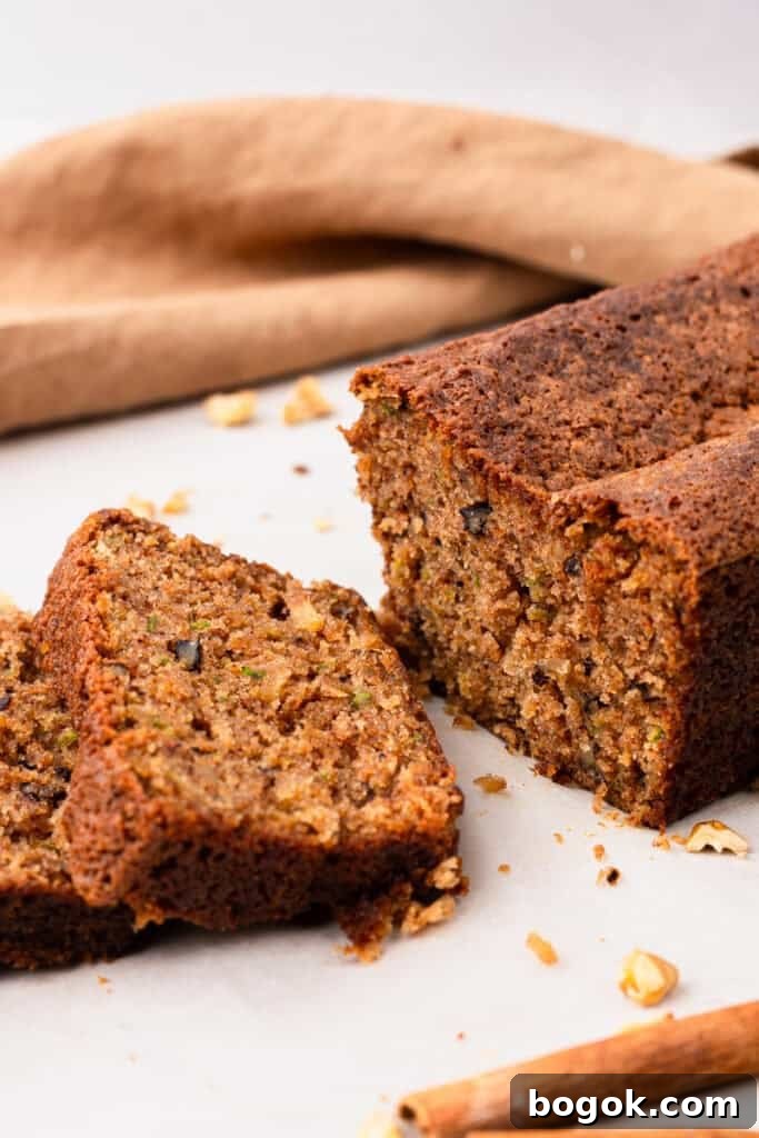 Ultra-Moist Gluten-Free Zucchini Bread with a Secret Ingredient 7 side view of Extra Moist Gluten Free Zucchini Bread on a plate with two slices cut out of the bread with crumbs on the plate