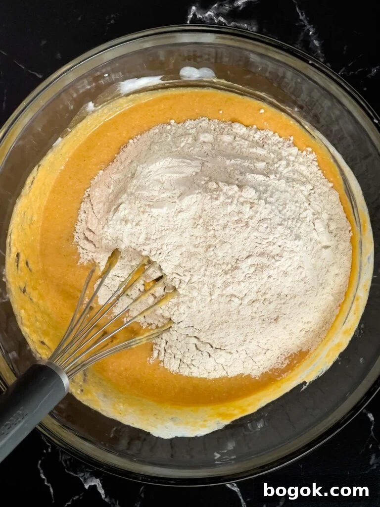 Dry ingredients added to the wet ingredients in a glass bowl for pumpkin pancakes.