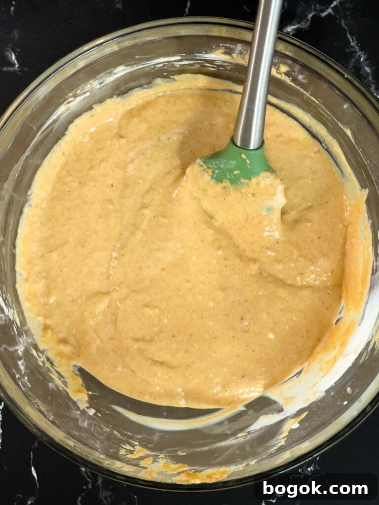 Pumpkin pancake batter mixed in a glass bowl on a dark surface.