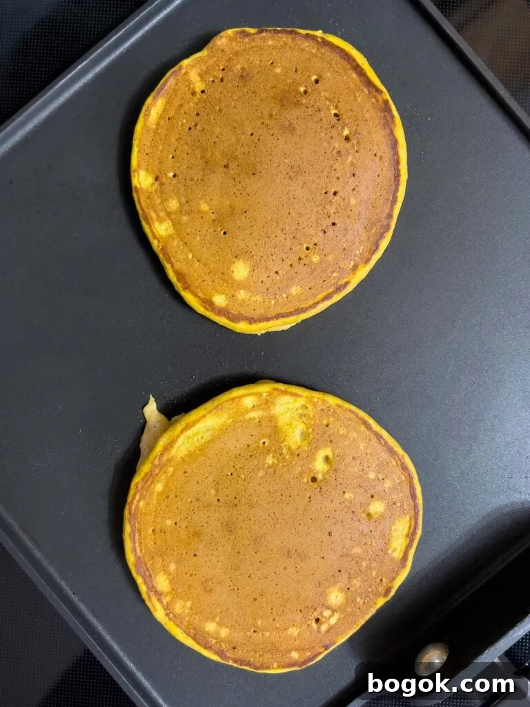 Pumpkin pancakes cooking on a griddle.