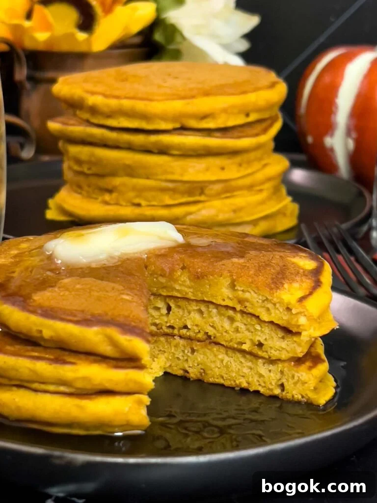 Stack of fluffy pumpkin pancakes with butter and maple syrup, golden edges on a dark plate.