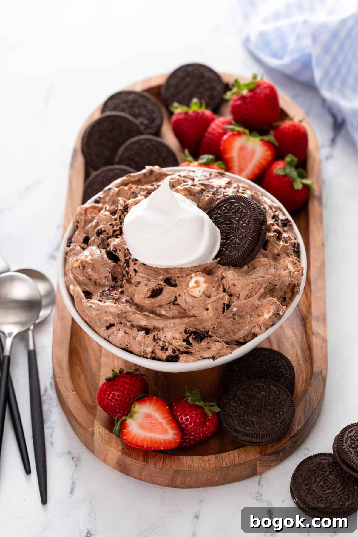 Bowl of oreo pudding topped with whipped cream and whole oreos, on a platter with oreos and fresh strawberries.