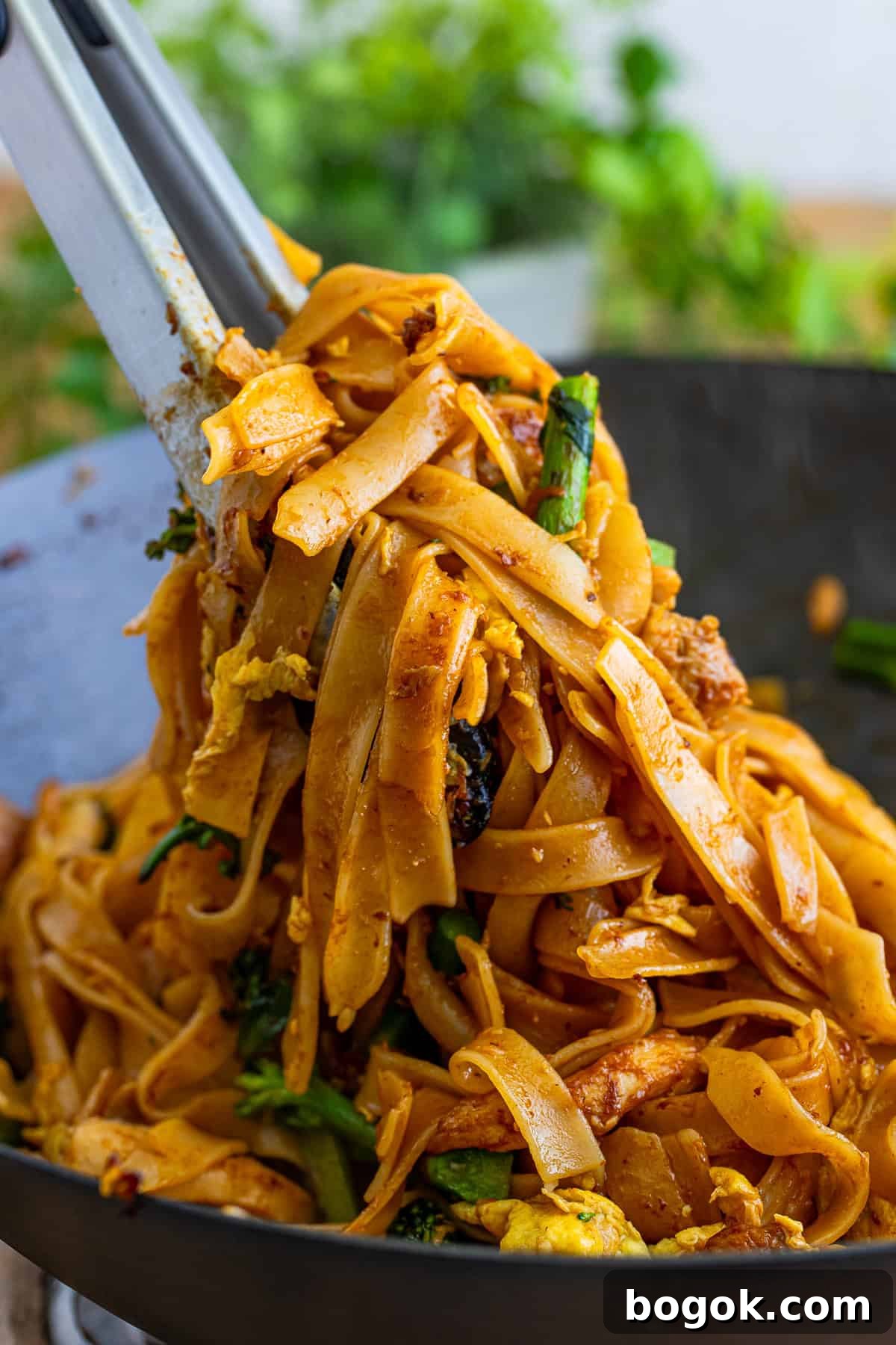 a pair of tongs grabbing some Thai Pad See Ew out of the wok