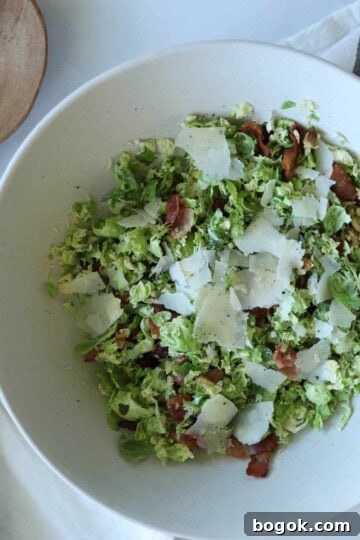 Shaved brussel sprout salad in salad bowl topped with parmesan cheese.