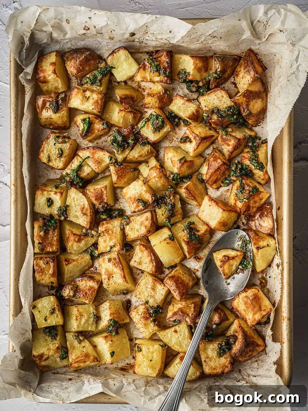Sheet pan with cooked cubed potatoes drizzled with the garlic herb sauce.