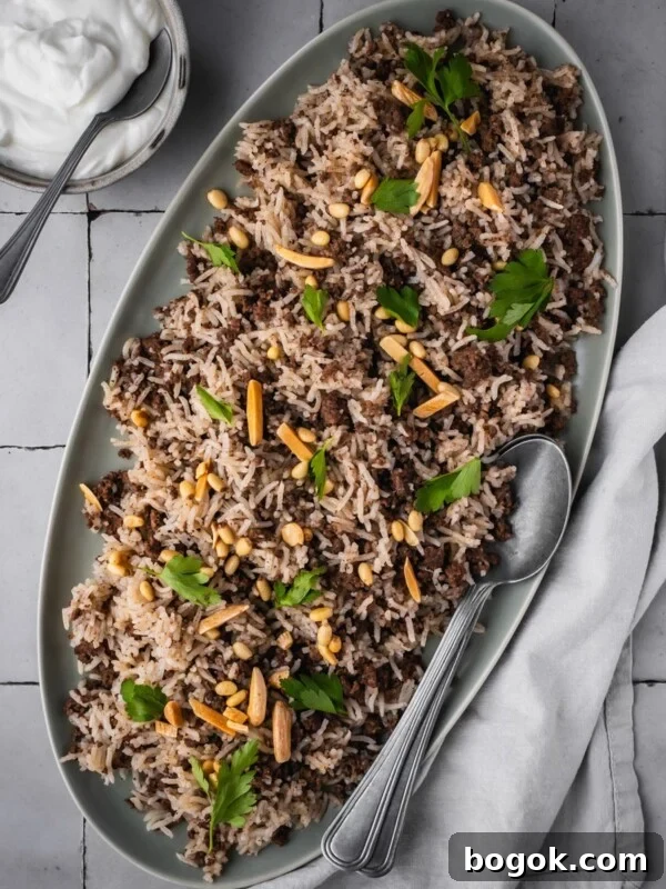 Platter with hashweh spiced rice with ground beef garnished with parsley and toasted nuts with a side of plain yogurt.