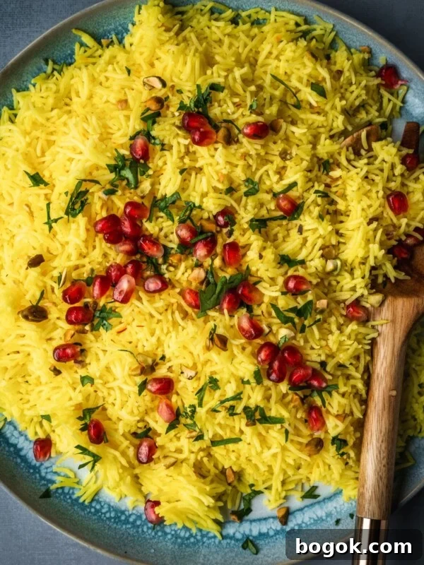 A plate with saffron rice garnished with pomegranate seeds, parsley and nuts.