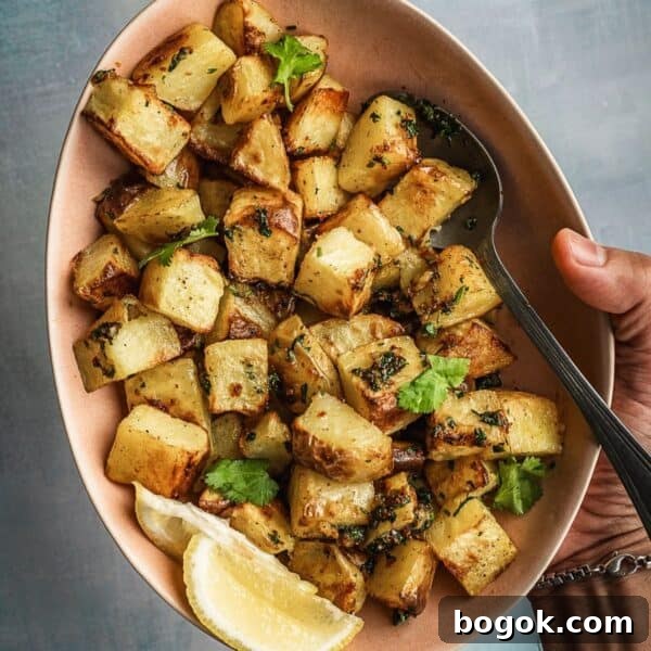 Bowl of spicy and herby potatoes with lemon wedges on the side.
