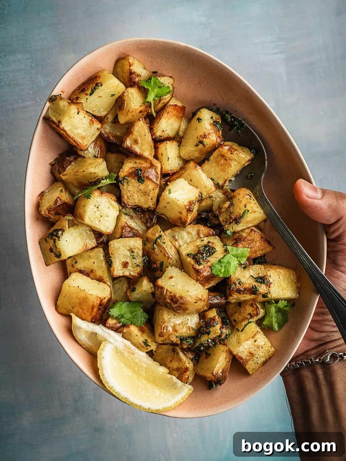 Bowl of spicy and herby potatoes with lemon wedges on the side.