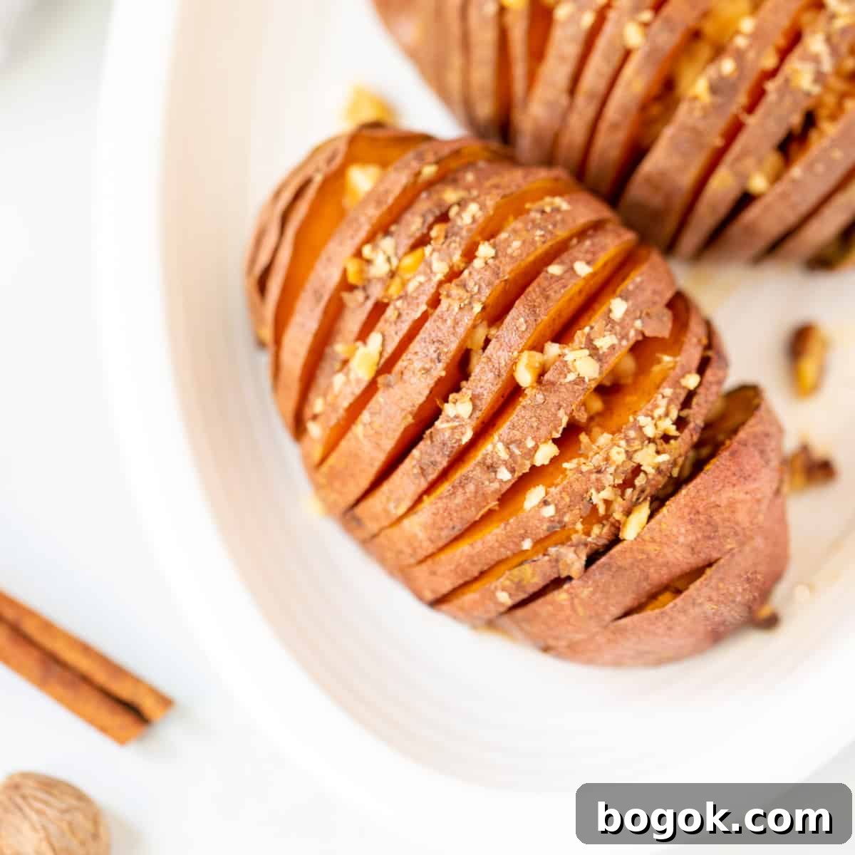 Simple Thanksgiving Recipes for a Stress-Free Holiday 2 Top down view of maple-glazed hasselback sweet potato on white platter.