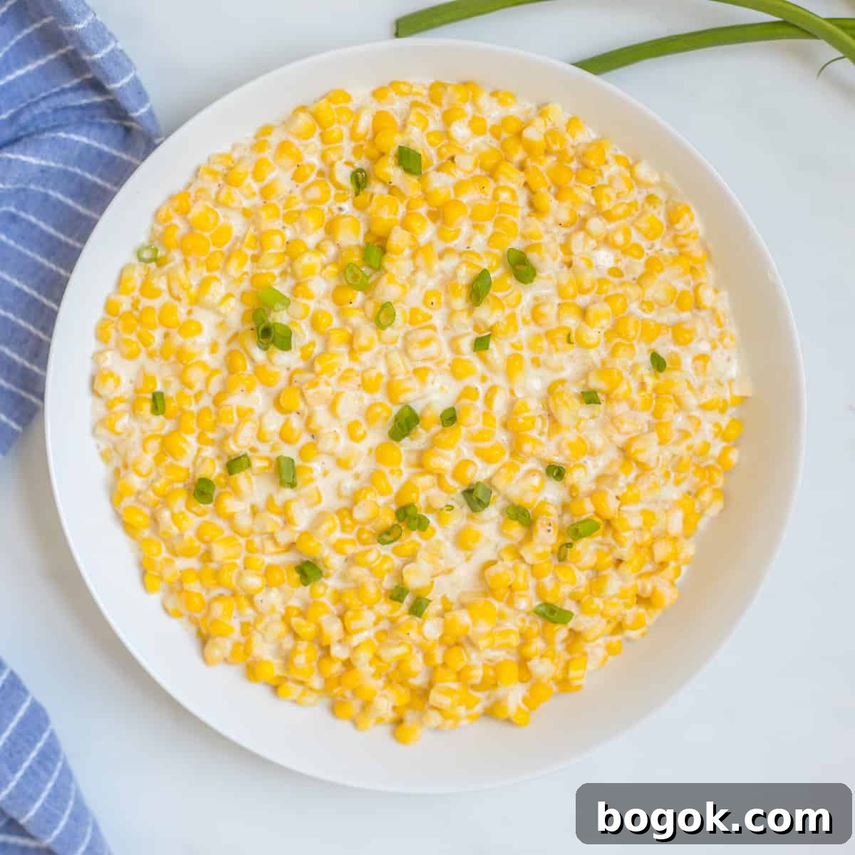 Easy Recipes for Thanksgiving White bowl filled with Instant Pot creamed corn topped with green onions next to blue towel.