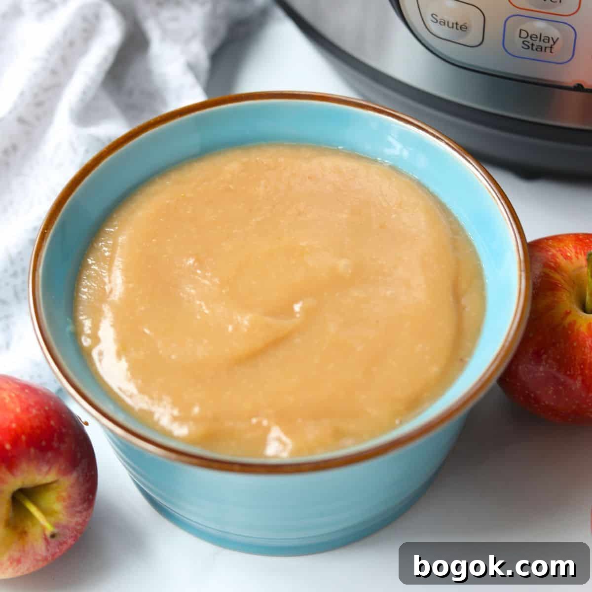 Easy Recipes for Thanksgiving Meal Instant Pot applesauce in blue bowl next to pressure cooker with apples in the background.