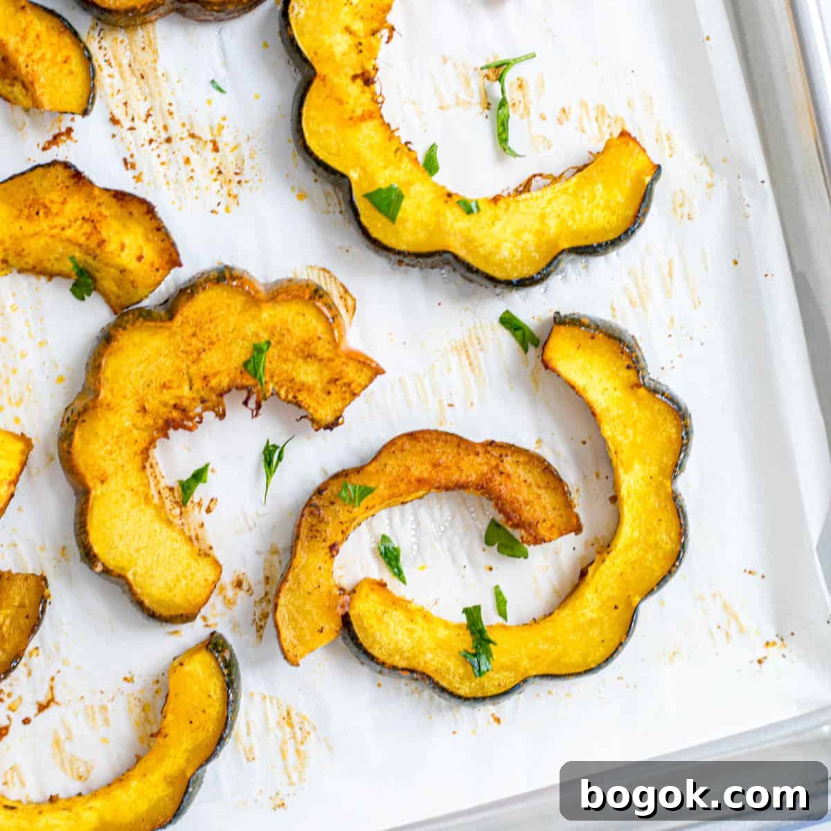 Thanksgiving Dinner Ideas Slices of Maple Roasted acorn squash on parchment paper topped with minced parsley.