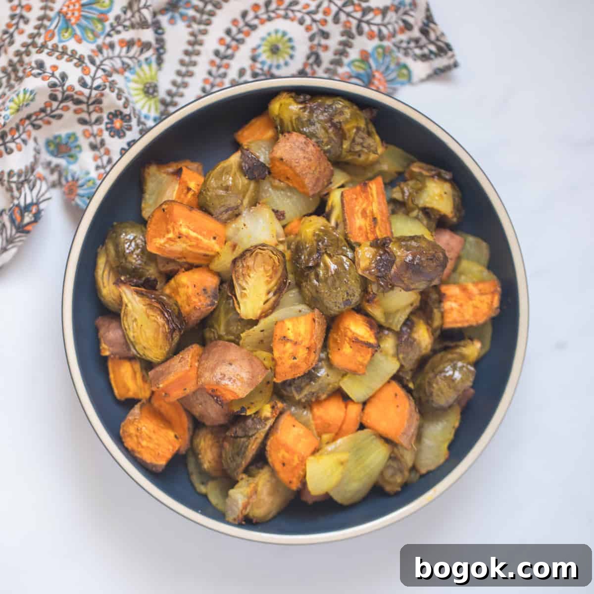 Easy Thanksgiving Dinner Ideas Roasted Fall Vegetables made with Brussels sprouts, onions, and sweet potatoes in blue bowl.