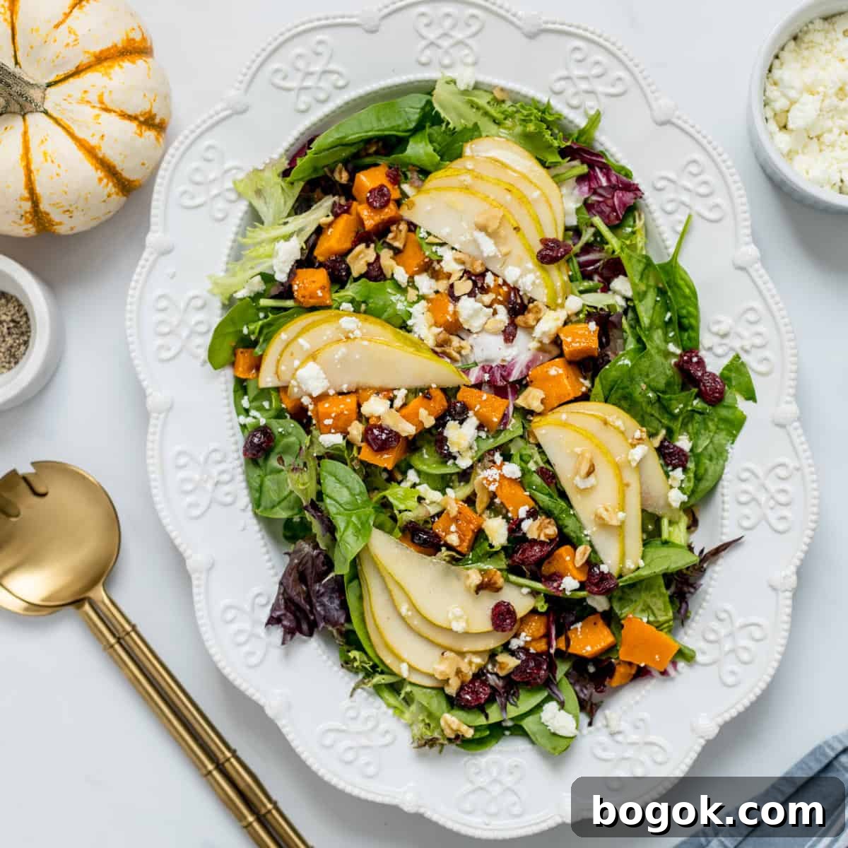 Easy Ideas for Thanksgiving Meal Salad on white platter made with mixed greens, roasted butternut squash, dried cranberries, feta and pears.