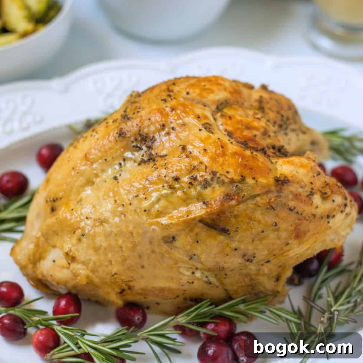 Thanksgiving Recipes Easy Instant pot turkey breast on white platter with crispy skin surrounded by rosemary sprigs and cranberries.