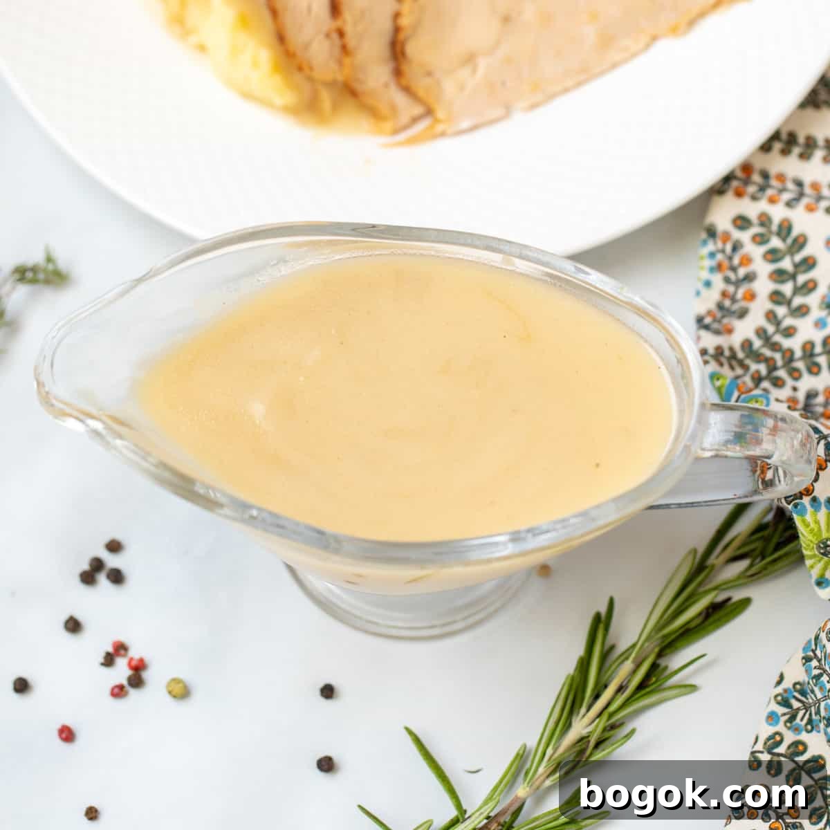 Easy Recipes for Thanksgiving Turkey gravy in clear gravy bowl next to fresh herbs.