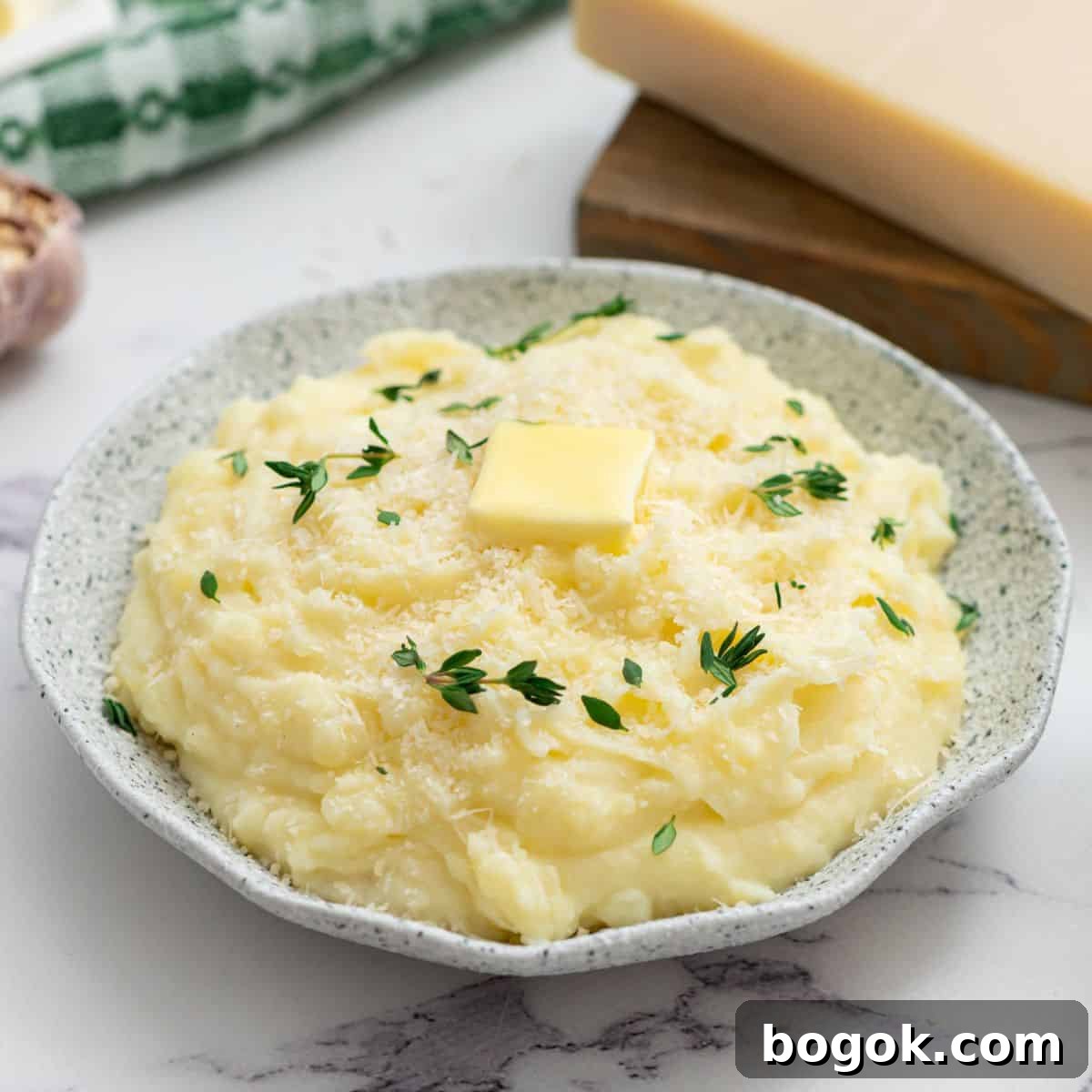 Easy Thanksgiving Recipes Crockpot mashed potatoes in serving bowl topped with parmesan, butter, and thyme.