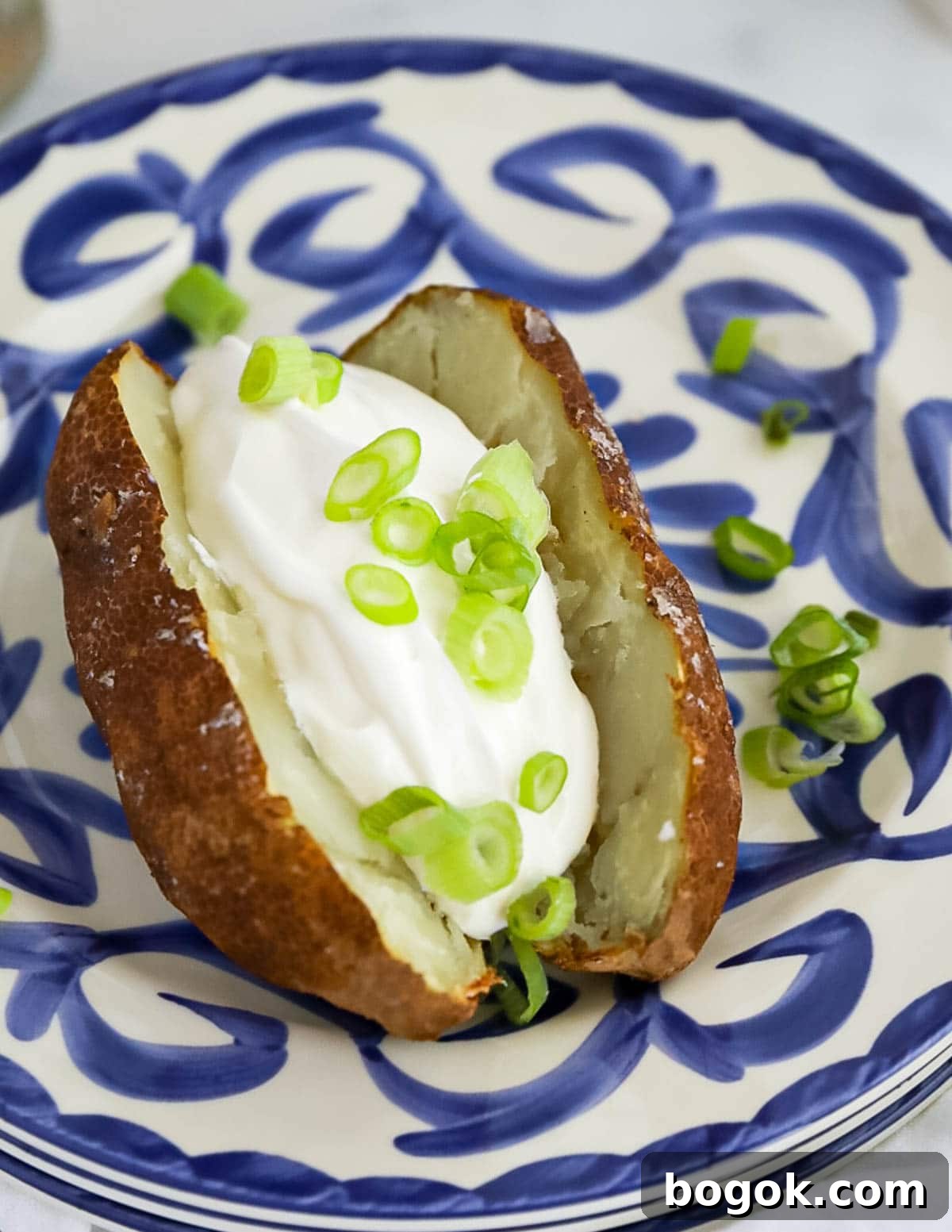 A sliced russet potato with a scoop of sour cream and sliced green onions in the potato.