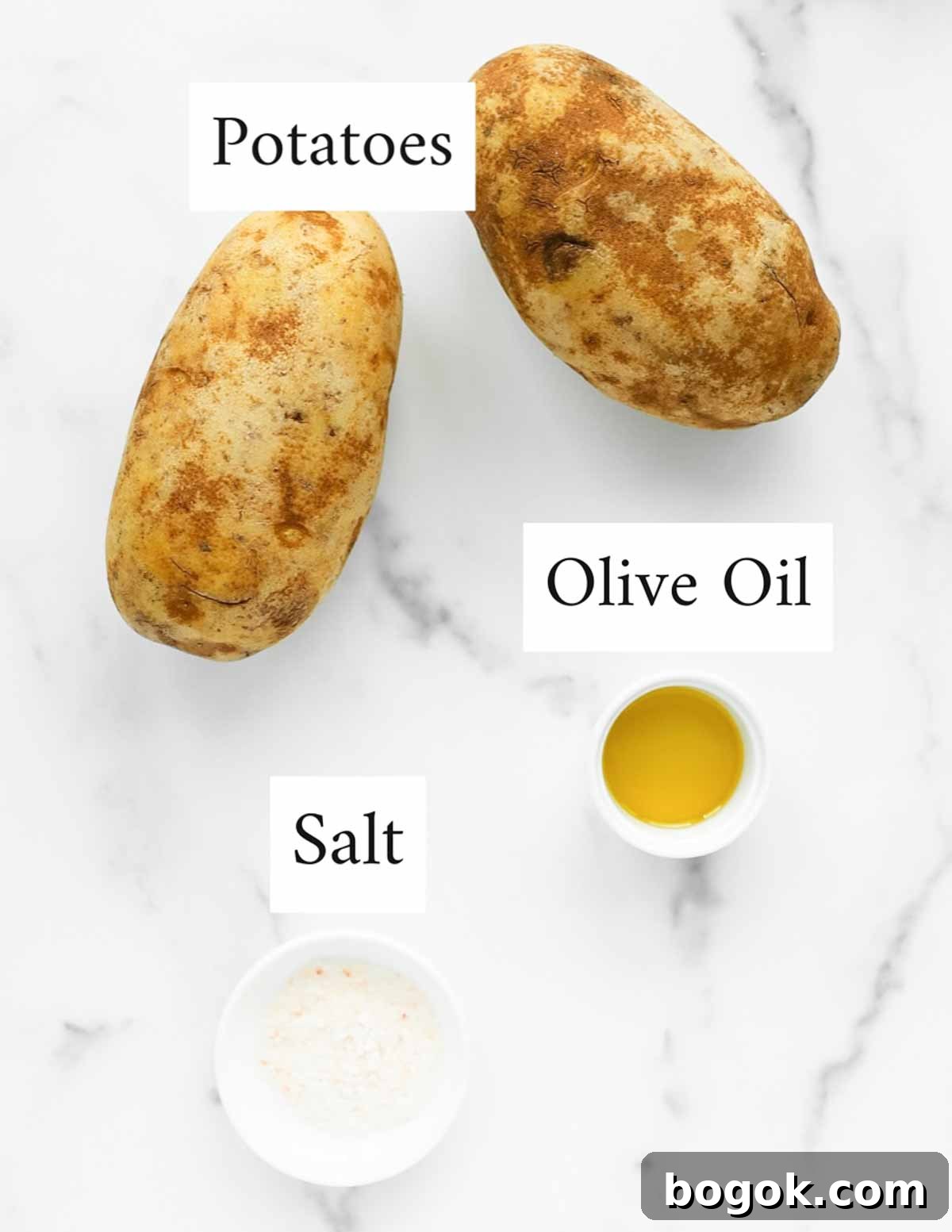 an overhead image of two potatoes, a small white dish containing olive oil, and a small white dish containing salt