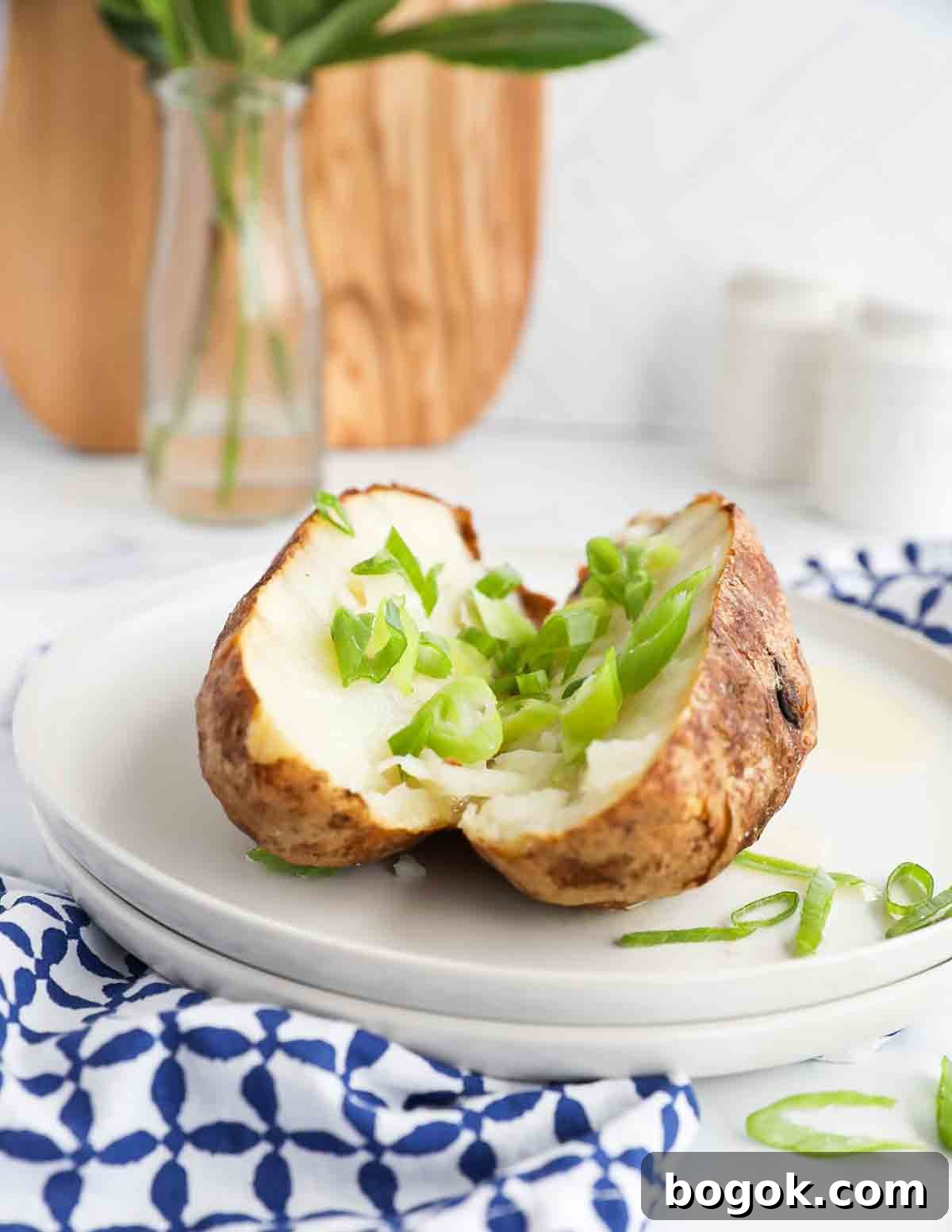 A sliced baked potato covered in sliced green onions on two stacked white plates.