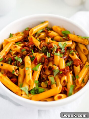 A white bowl filled with penne covered in a red sauce and topped with fresh green basil