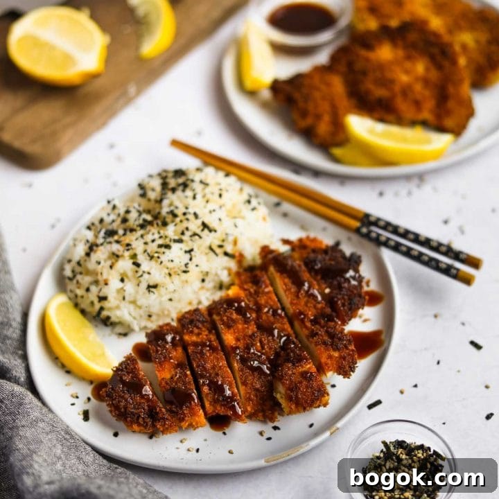 Chicken Katsu (Japanese Chicken Cutlet) on a plate with rice with lemon slices and and furikake.
