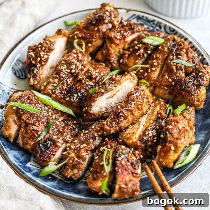 Miso jidori chicken thighs topped with sesame seeds and sliced green onions on a blue ceramic Japanese plate.