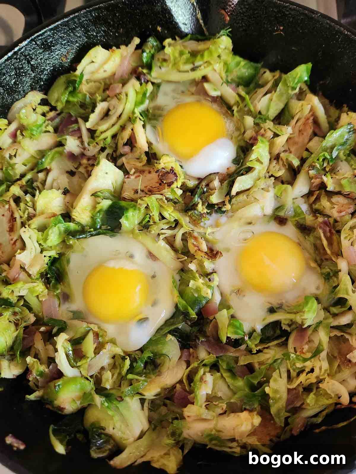 Crispy Brussels Sprout Hash with Bacon and Caramelized Onions 9 Brussel sprouts in a black skillet with 3 eggs in it.