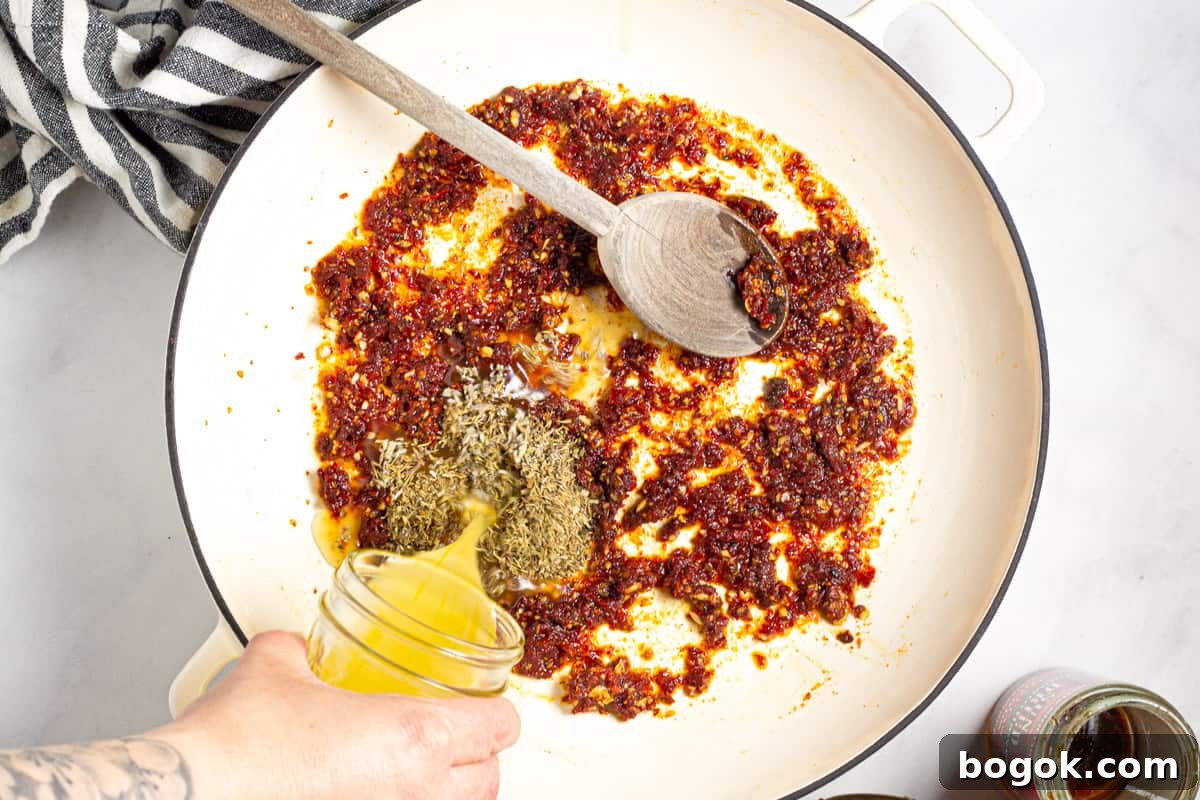 15-Minute Cream Tomato Pasta with Garlic and Basil 5 Chicken broth being poured into a pan of minced sun dried tomato.
