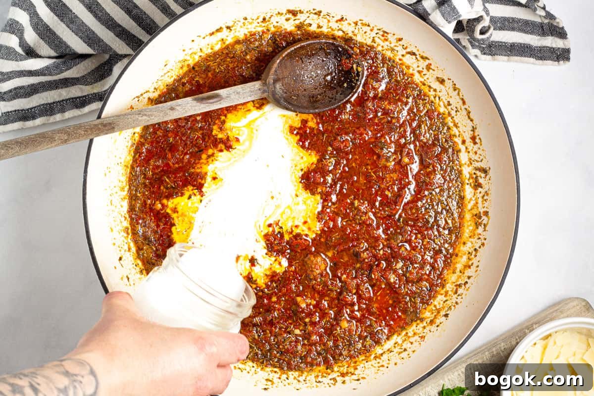 15-Minute Cream Tomato Pasta with Garlic and Basil 6 Heavy cream being poured into a pan of sun-dried tomato sauce.