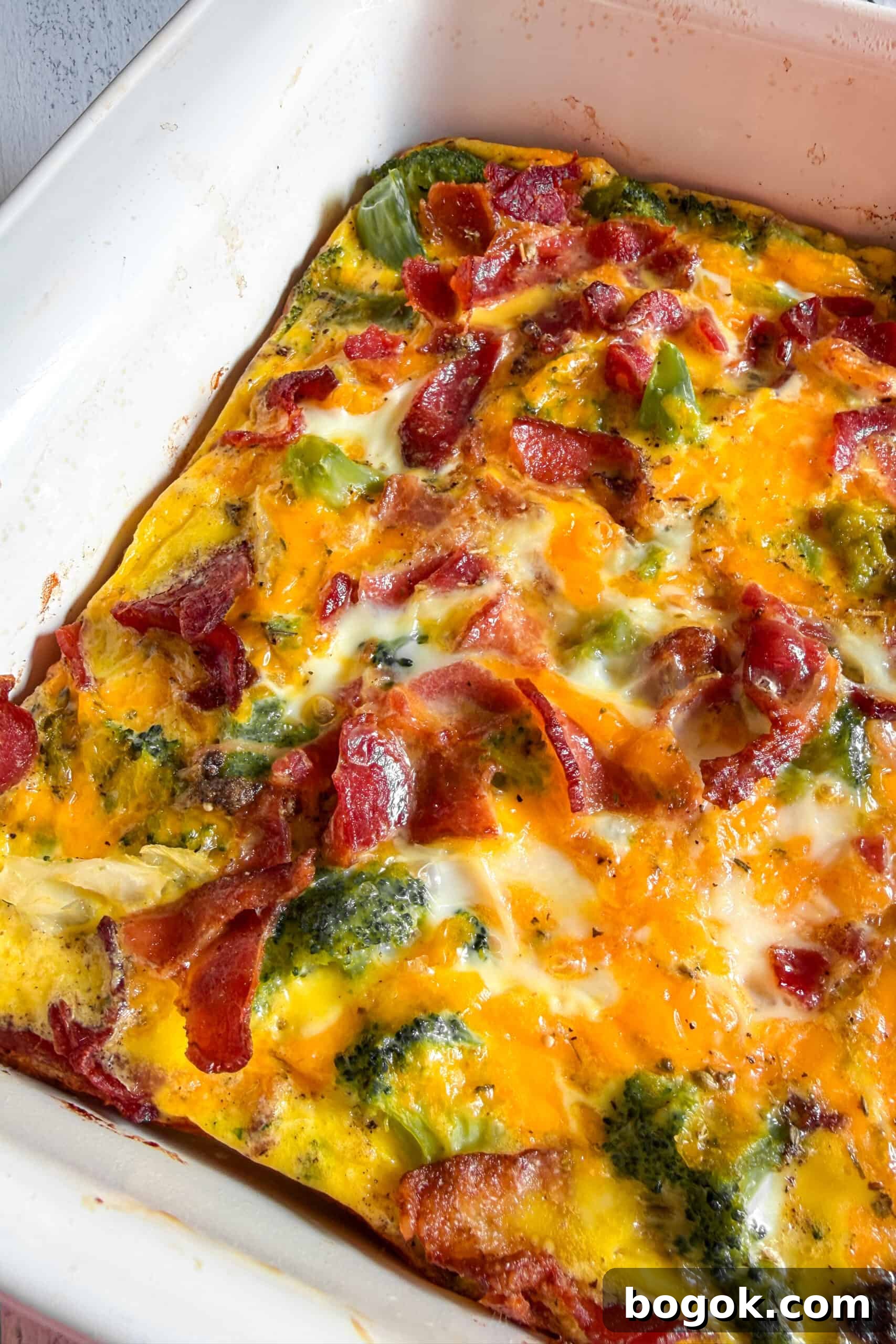 Low-Carb Bacon and Broccoli Breakfast Casserole 2 Low carb bacon broccoli breakfast casserole sliced in a baking dish with cheddar cheese and crispy bacon on top.