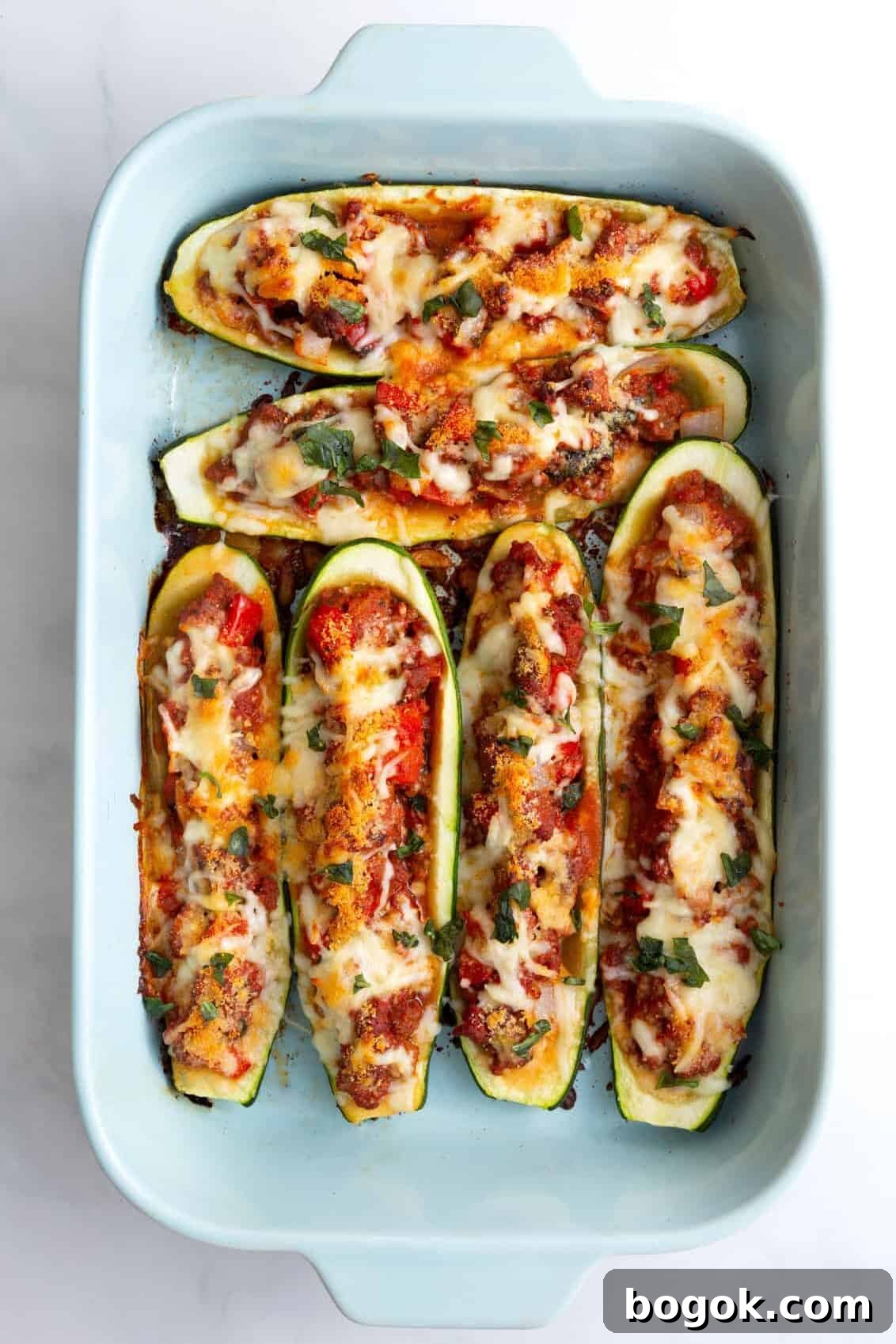 cooked stuffed zucchini boats sitting in a blue 9x13 casserole dish.
