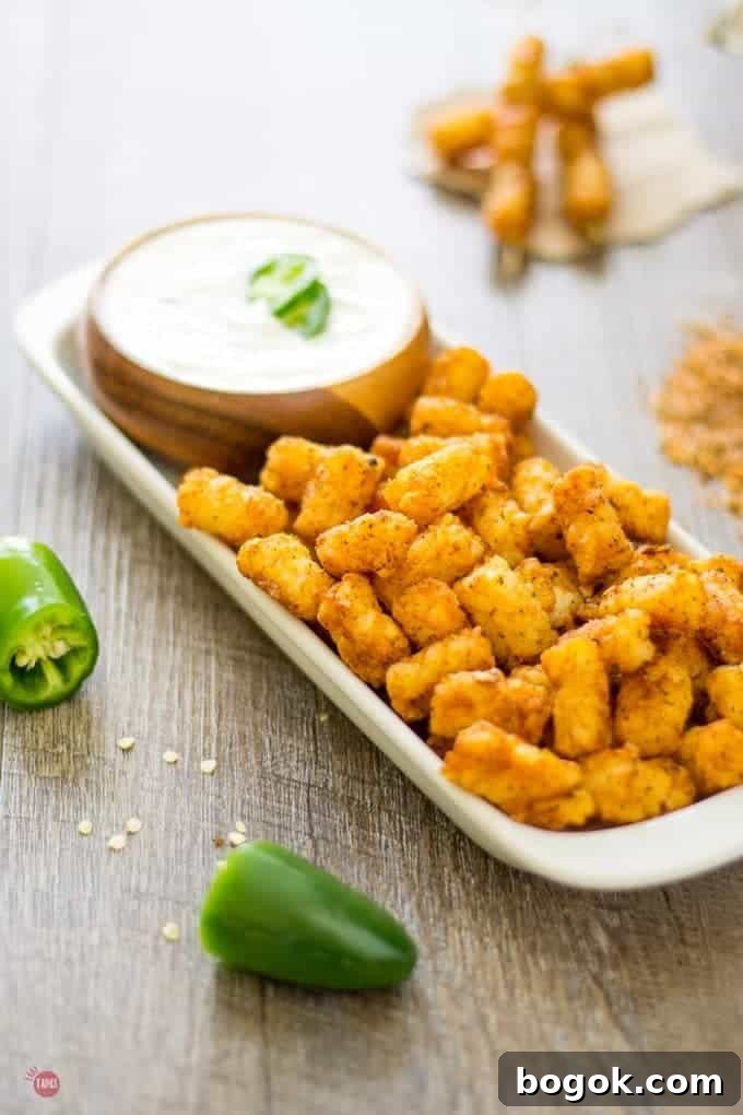 Steakhouse tater tots and jalapeno ranch dip in a wood bowl all on a white platter.