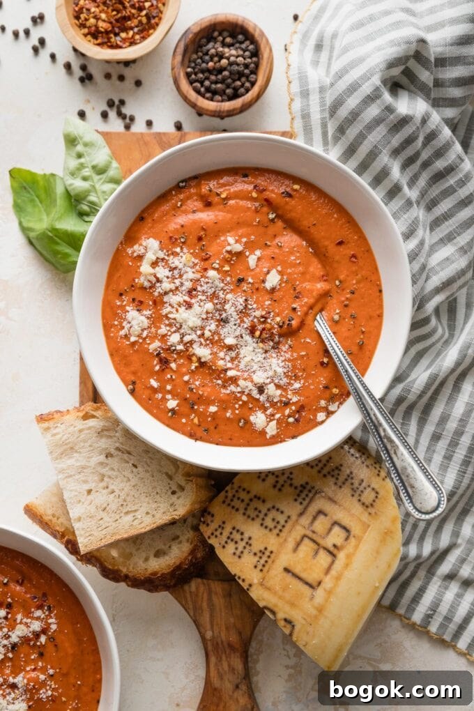 Countertop set with bowls of tomato butternut bisque, sliced sourdough bread, and garnishes of herbs and fresh Parmesan.