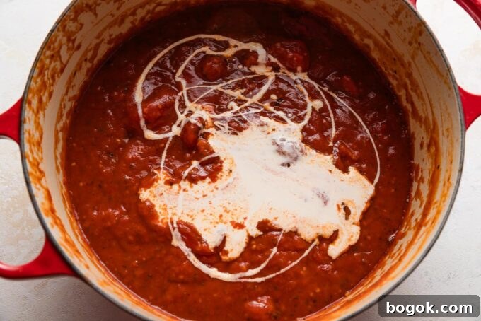 Cream just poured but not yet mixed into a tomato soup base in an extra large Dutch oven.