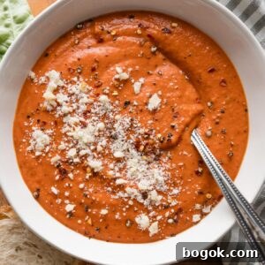 Bowl of tomato bisque with butternut squash garnished with a generous sprinkle of Parmesan cheese and fresh-cracked black pepper.