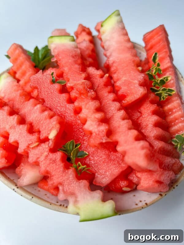 A bowl filled with crinkle-cut watermelon fries, garnished with small green herb sprigs, on a light background—making for a refreshing and fun watermelon snack.