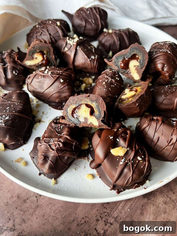 A plate of Chocolate Covered Dates, some cut open to reveal a creamy peanut butter filling, sprinkled with bits of sea salt and crunchy nuts.