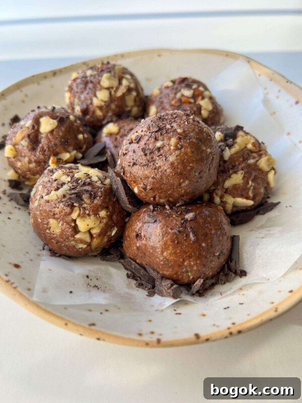 A plate with seven chocolate Energy Balls rolled in chopped nuts, resting on parchment paper and sprinkled with chocolate shavings.