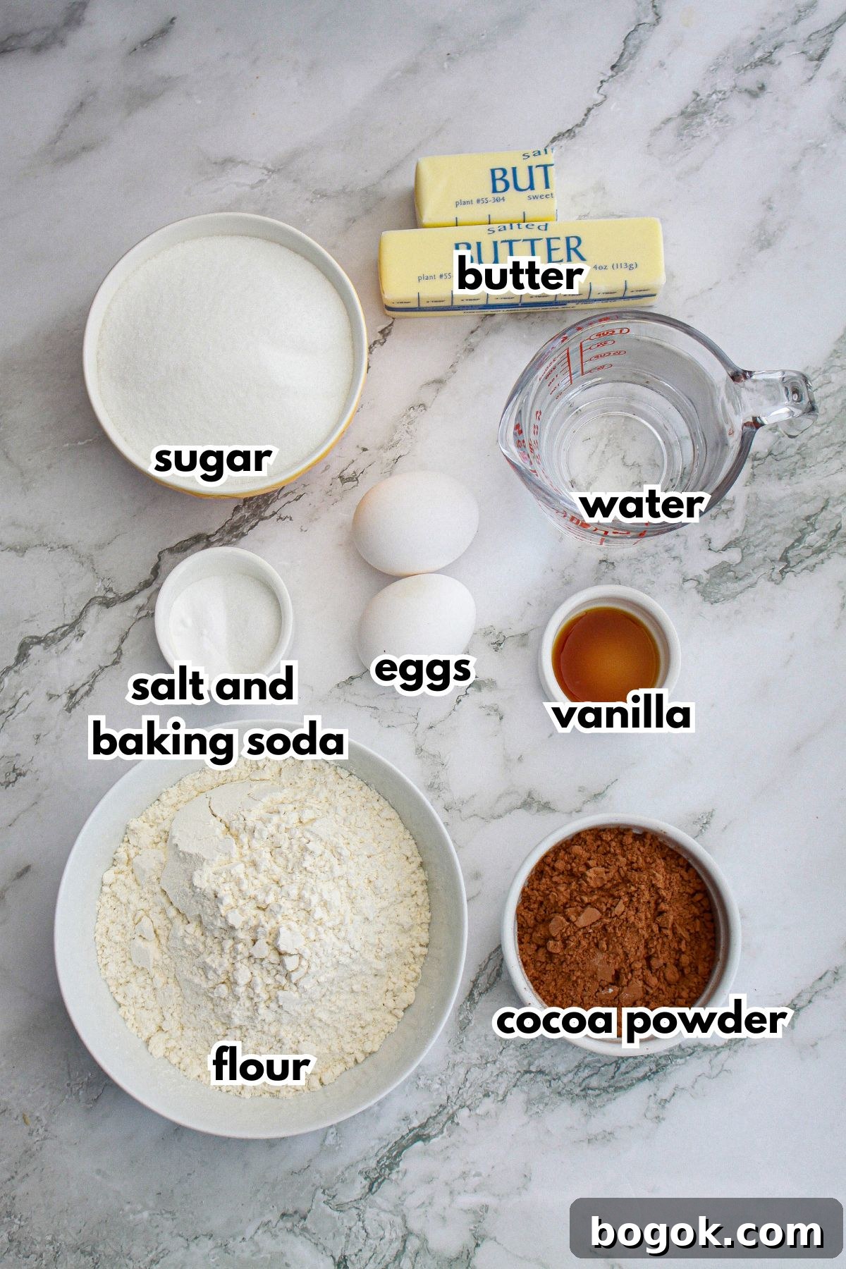 bowls of butter, sugar, salt, baking soda, eggs, vanilla, flour, cocoa powder, and water on a counter.