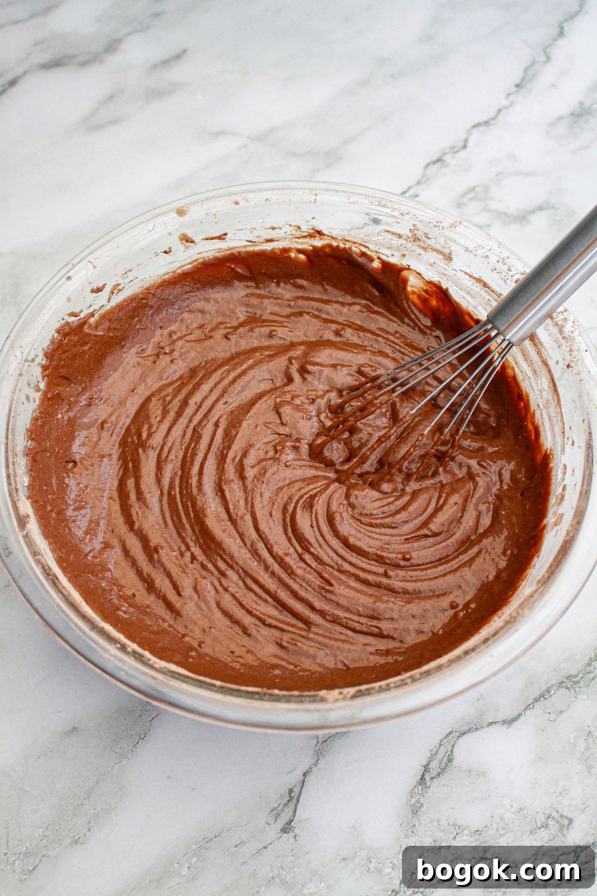chocolate cake batter in a glass mixing being stirred with a whisk.