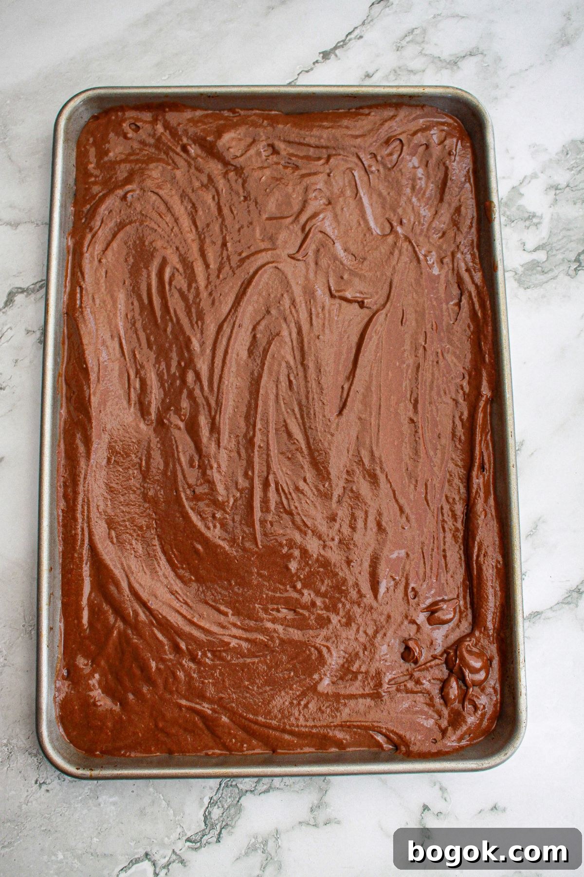 chocolate cake batter spread into a sheet pan ready for the oven.