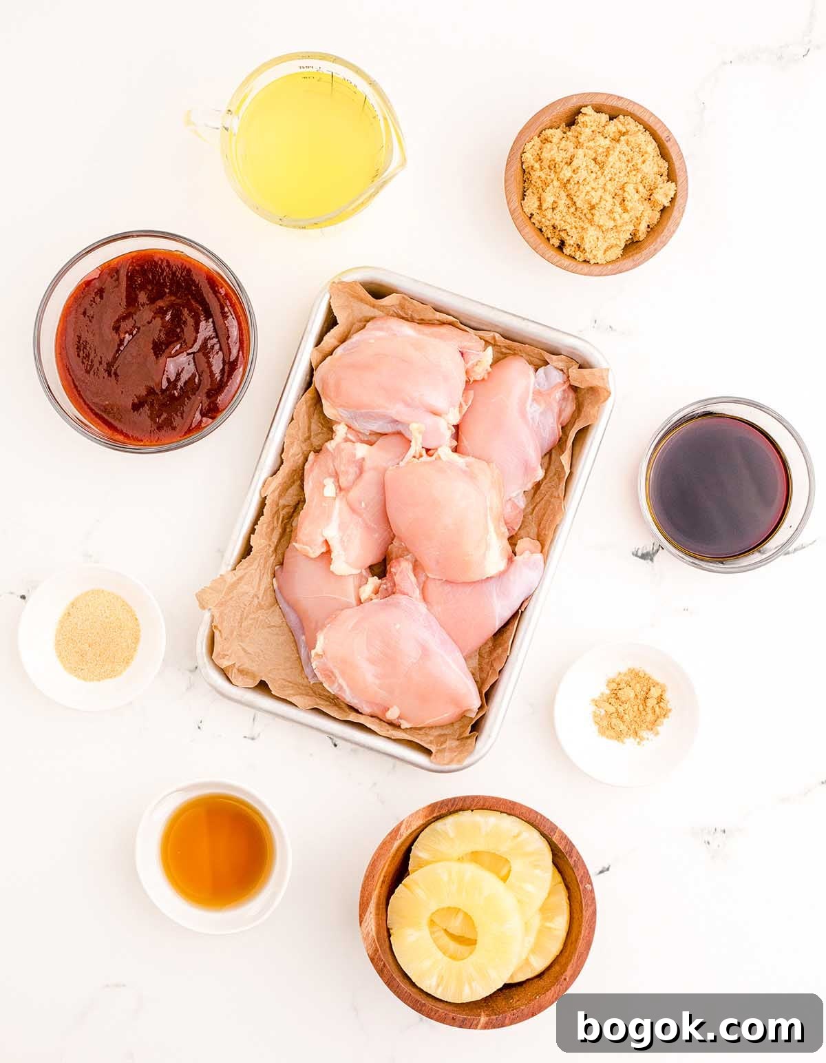 Hawaiian-Style BBQ Chicken with Pineapple Glaze 13 Raw chicken thighs are surrounded by bowls containing barbecue sauce, pineapple slices, brown sugar, olive oil, soy sauce, garlic powder, ginger, and apple cider vinegar on a white surface—perfect for creating a mouth-watering Hawaiian BBQ Chicken feast.
