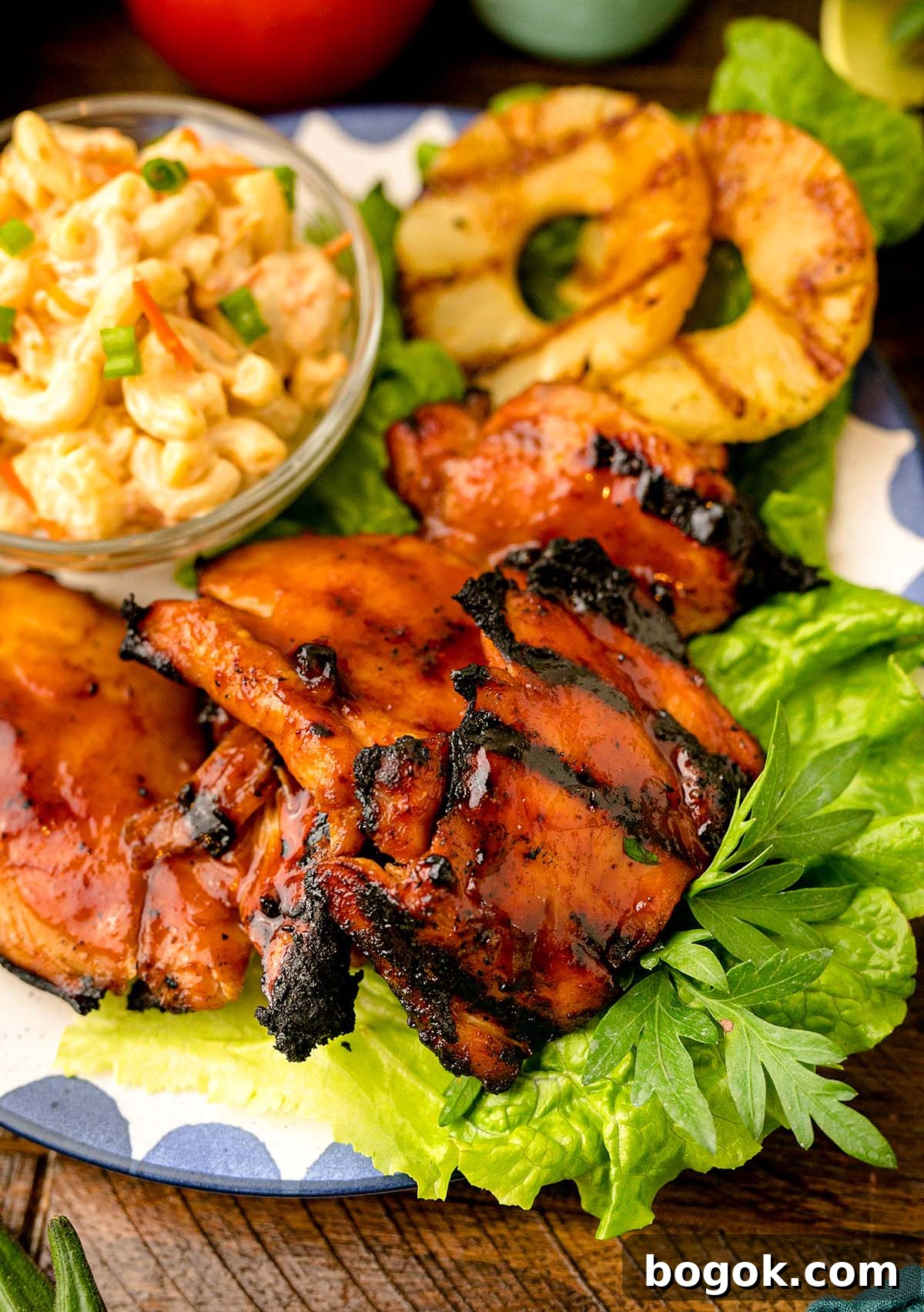 Hawaiian-Style BBQ Chicken with Pineapple Glaze 4 Savor the Hawaiian BBQ chicken, grilled to perfection on a bed of lettuce with grilled pineapple slices, accompanied by a delicious side of macaroni salad on a plate.